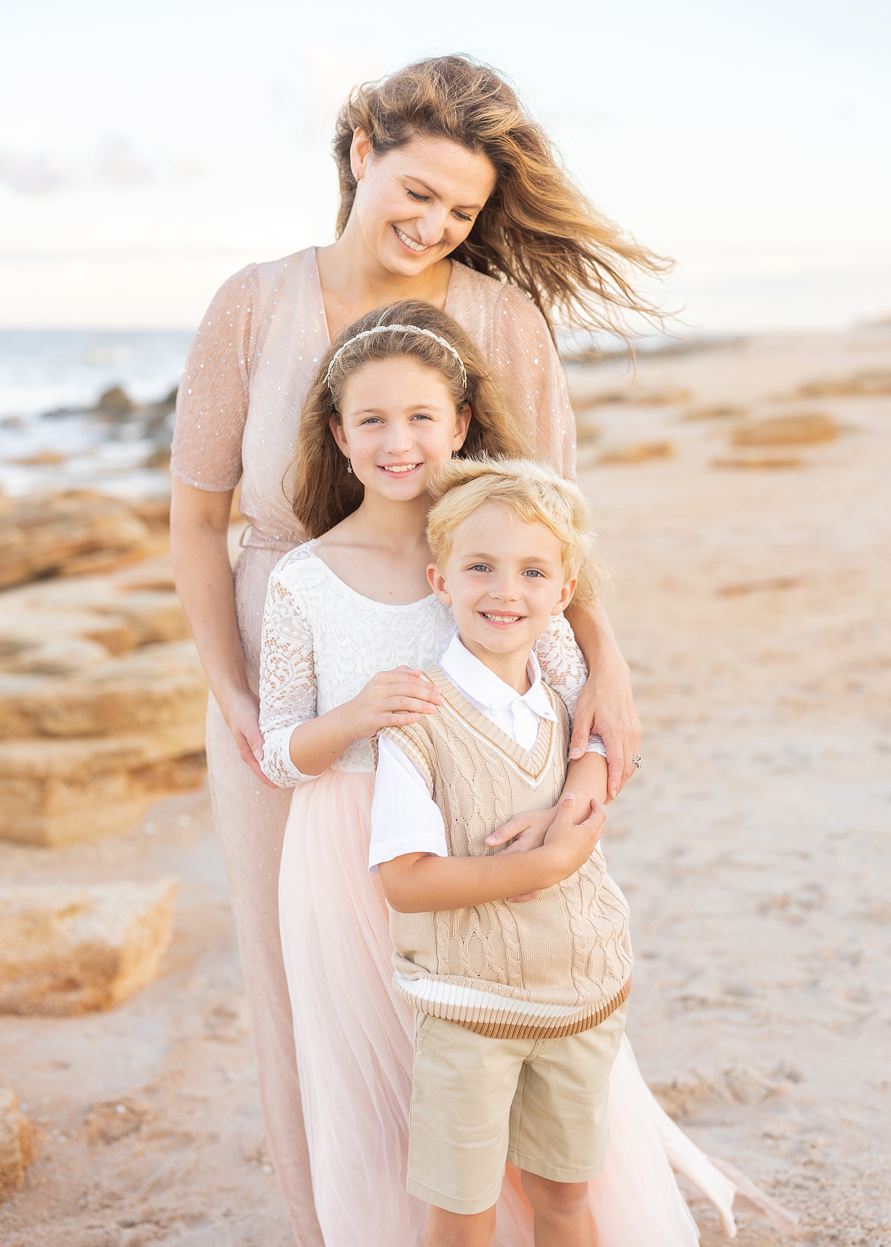 woman wearing gold dress on the beach at sunset holding her two children