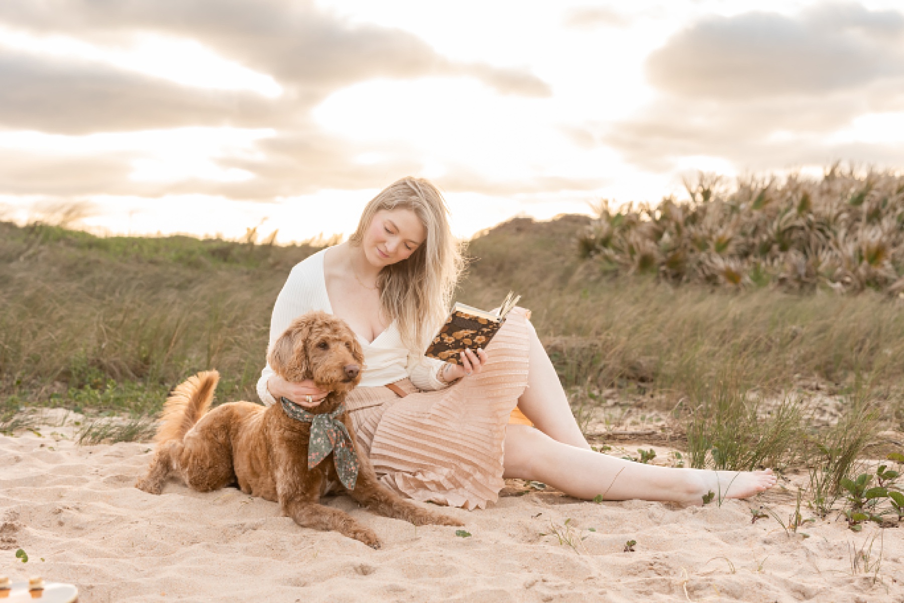 woman in pink pleated skirt sitting on the sand with dog at the beach