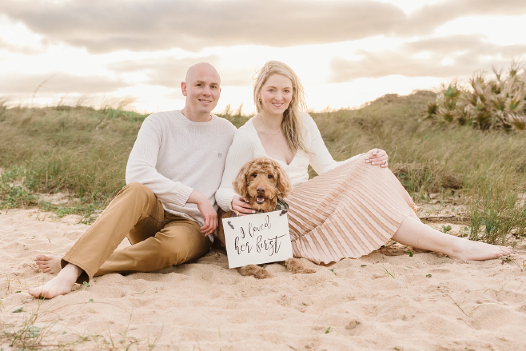couple at the beach with golden doodle and sign