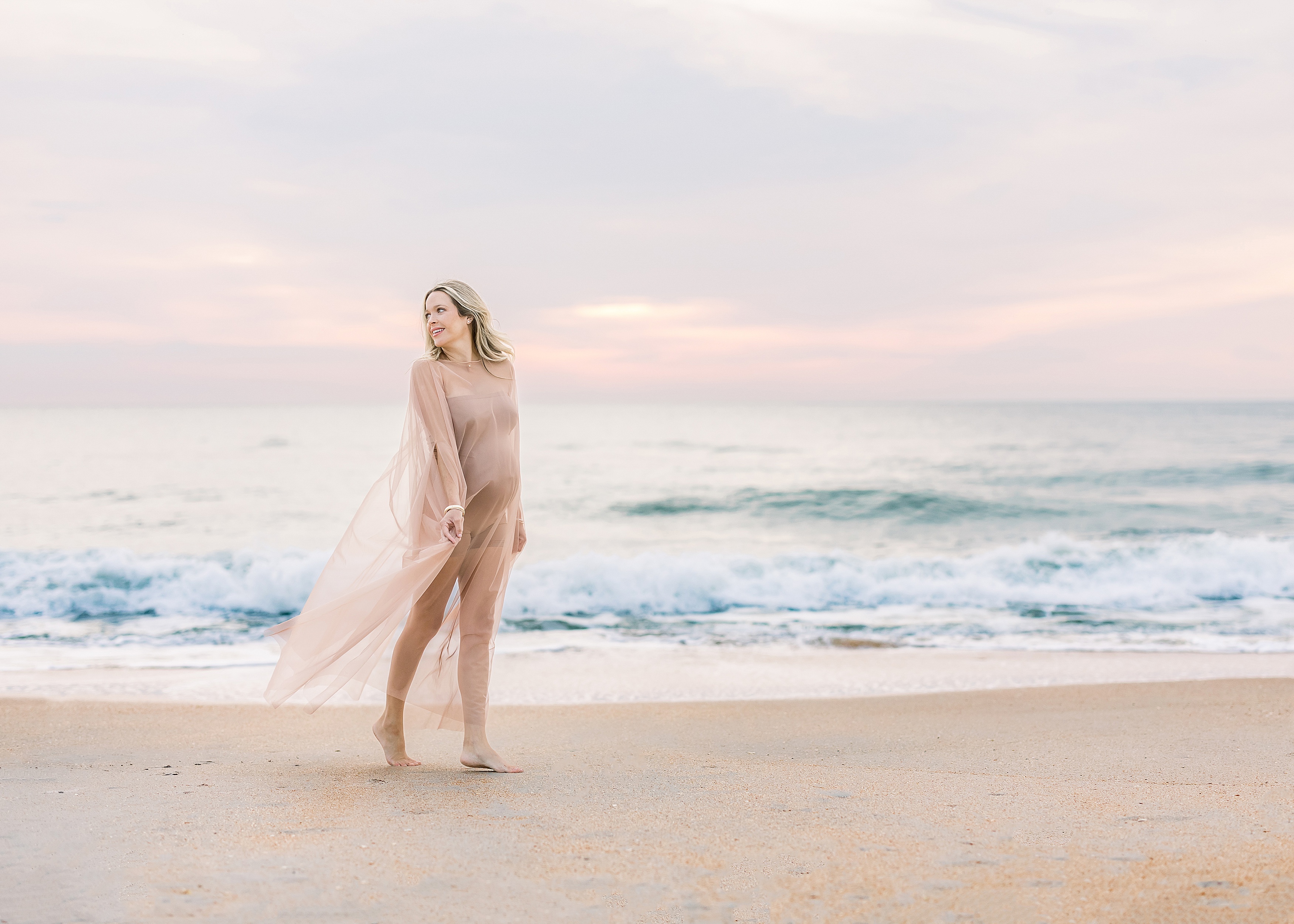 blond pregnant woman in sheer nude dress standing on the beach at sunrise in Saint Augustine Florida
