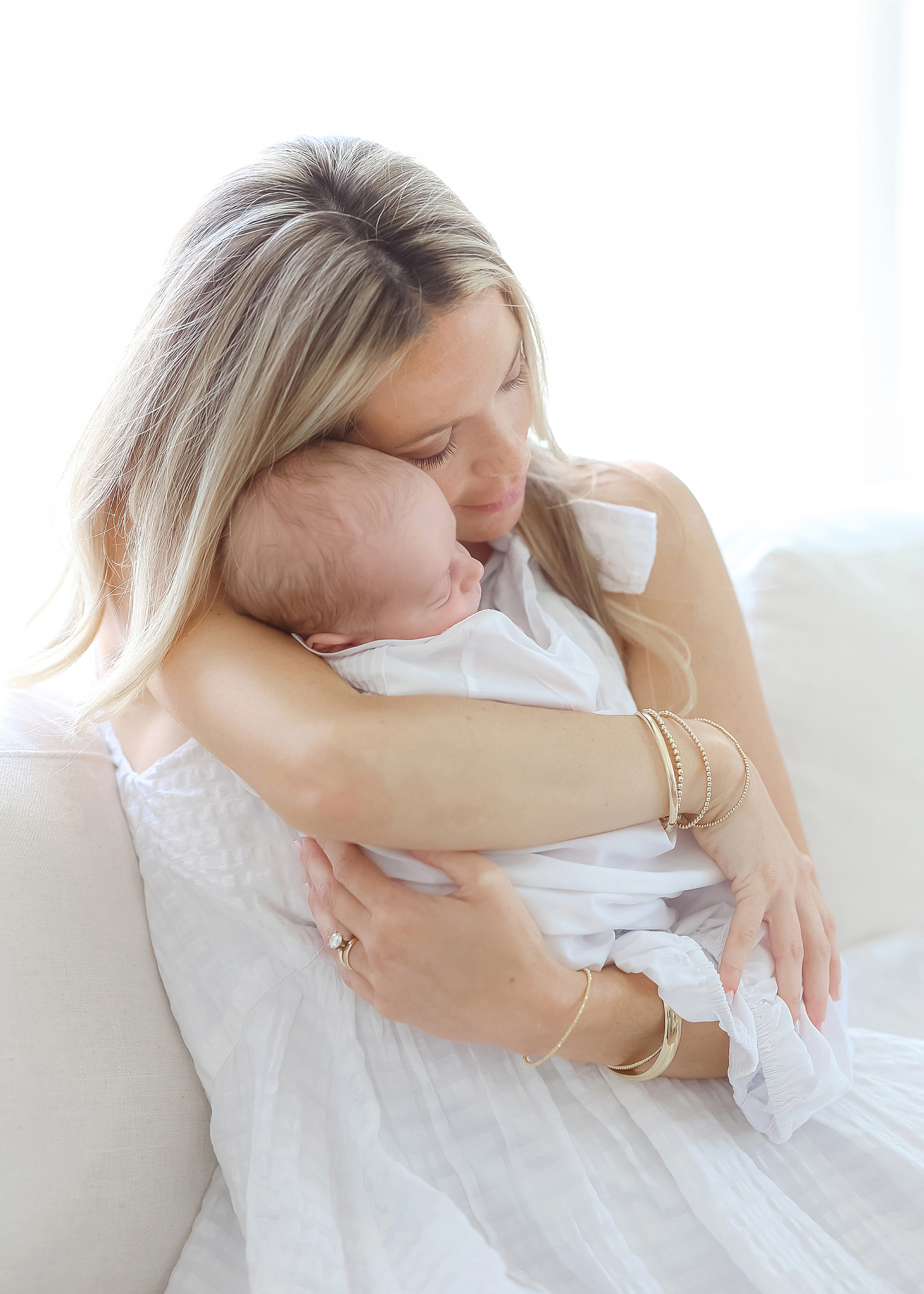 Light and airy at home newborn portrait of woman holding newborn baby boy dressed in white.