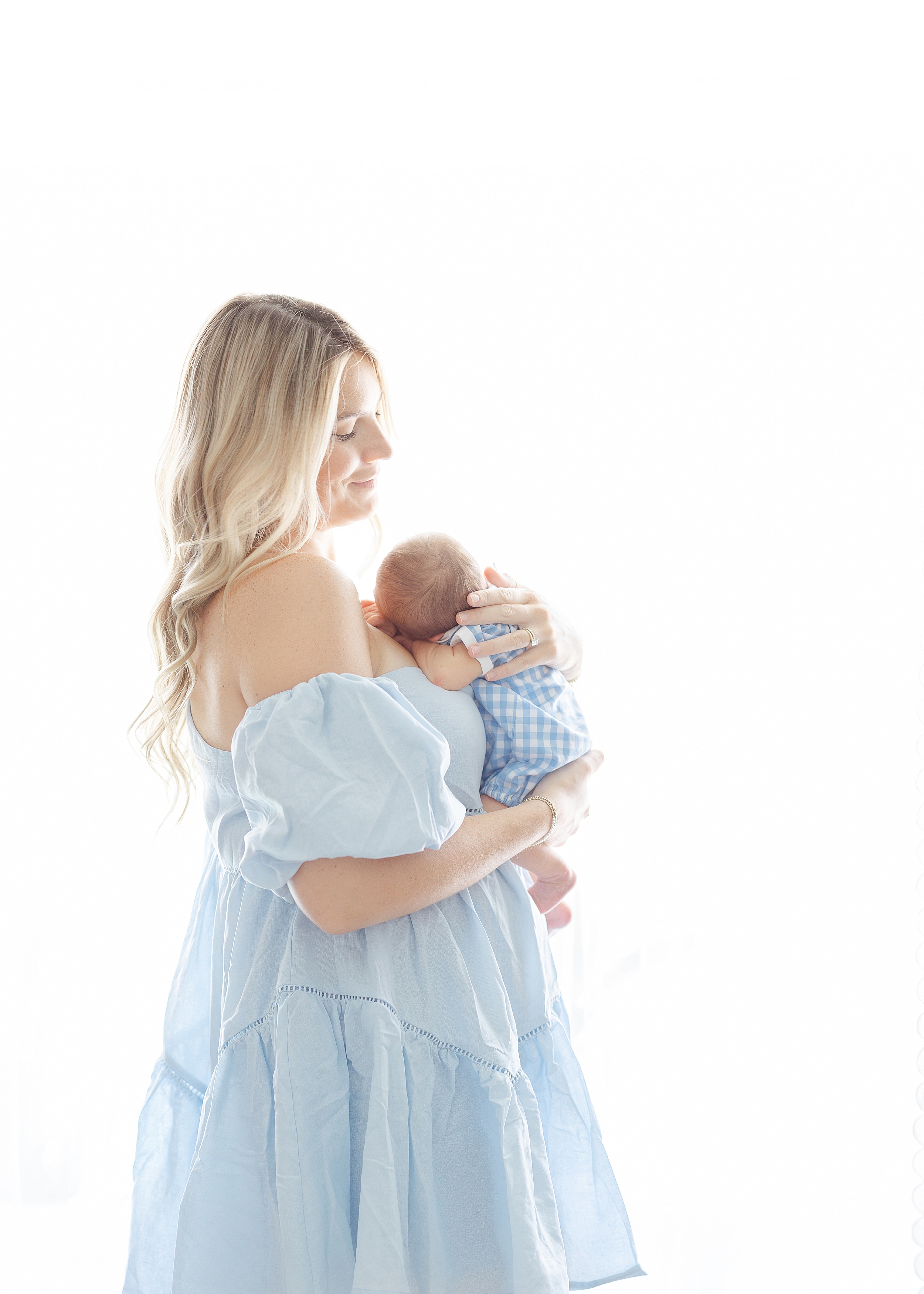 Light filled airy newborn portrait of blonde woman in pale blue dress holding baby boy.