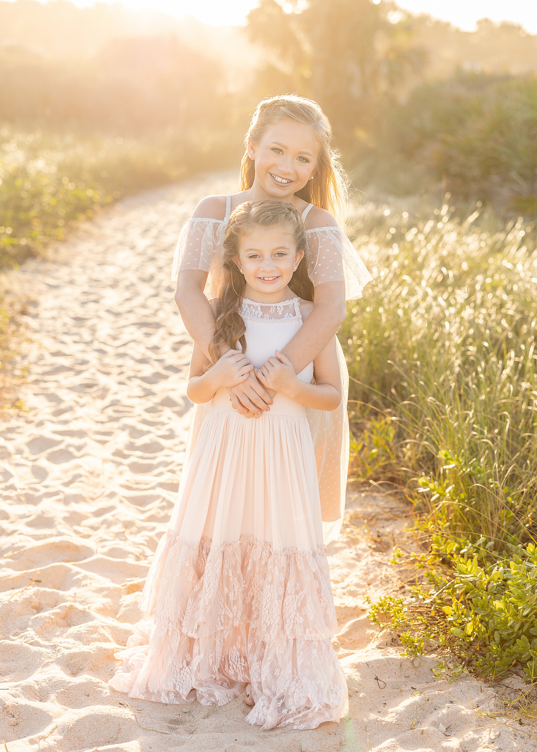 A light filled sunset portrait of two little girls in long dresses twirling with each other on St. Augustine Beach.