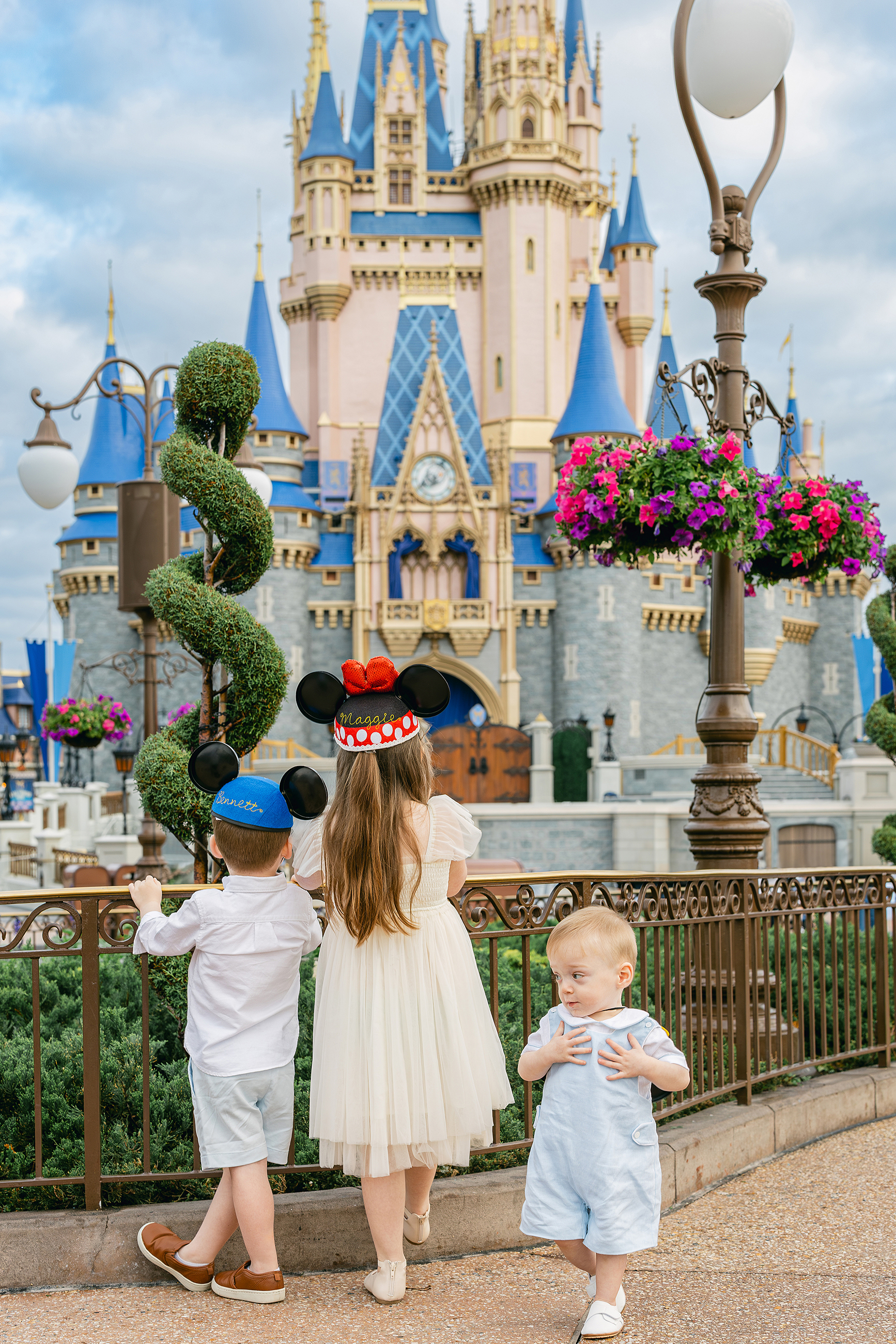 Three little children stand together in front of Cinderella's Castle at the Magic Kingdom.