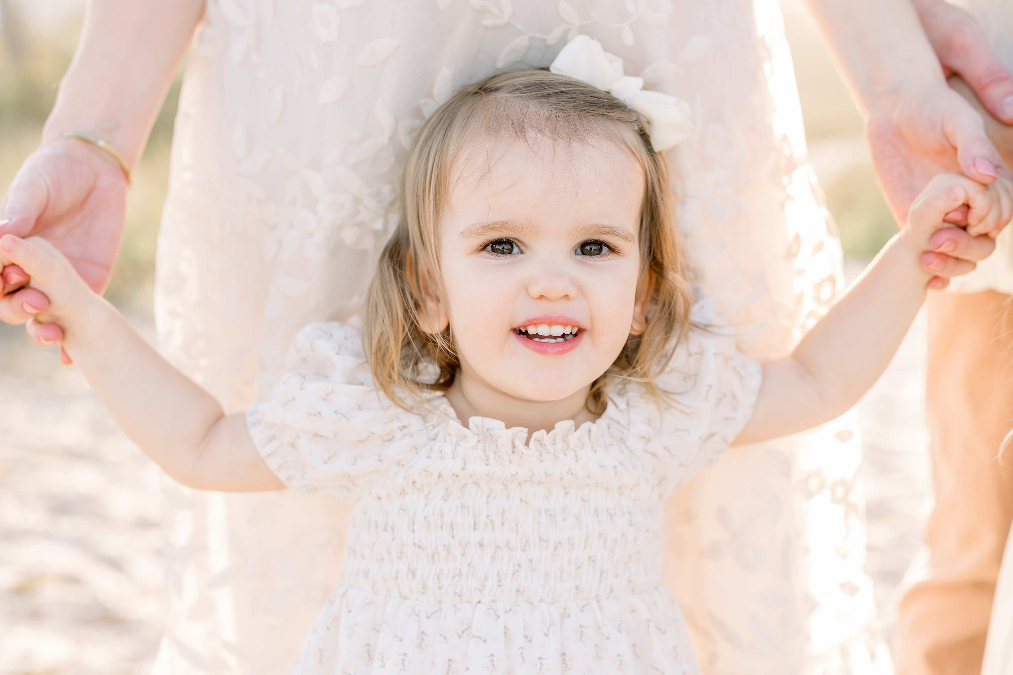 A light and airy beach portrait of a toddler girl wearing a cream dress.