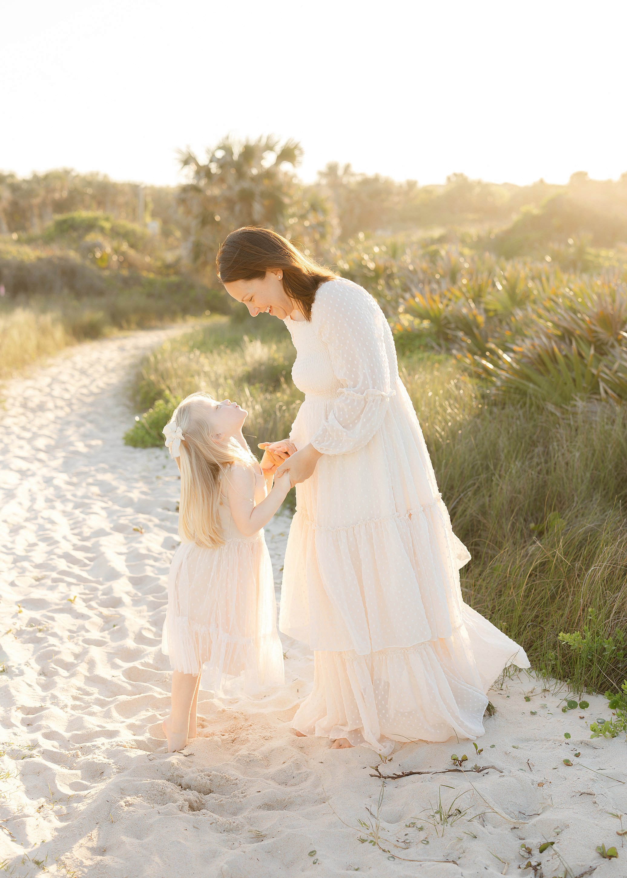 A light and airy golden portrait of a mother and daughter on the beach at sunset.