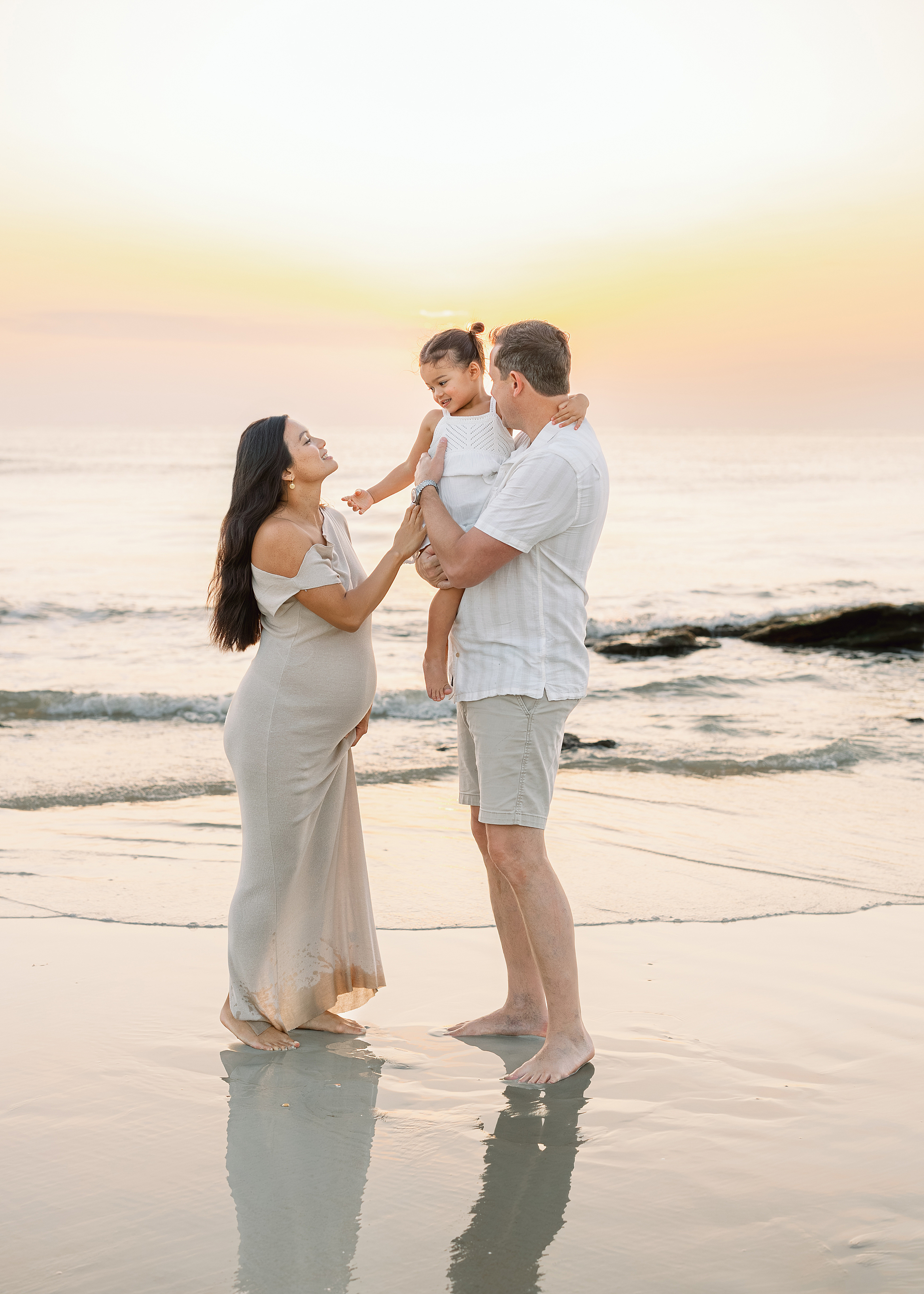 A family of three laughs with each other on St. Augustine Beach at sunrise.