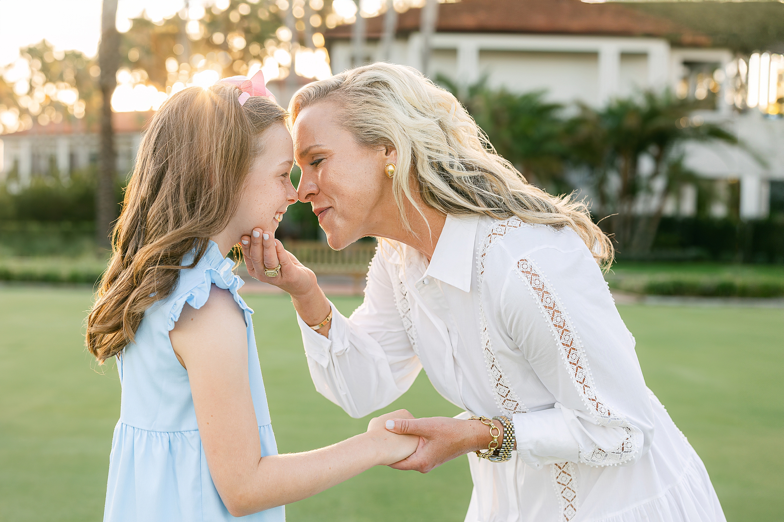 A woman in a white dress holds her little girl's face during a sunset on the golf course at Ponte Vedra Inn and Club. 