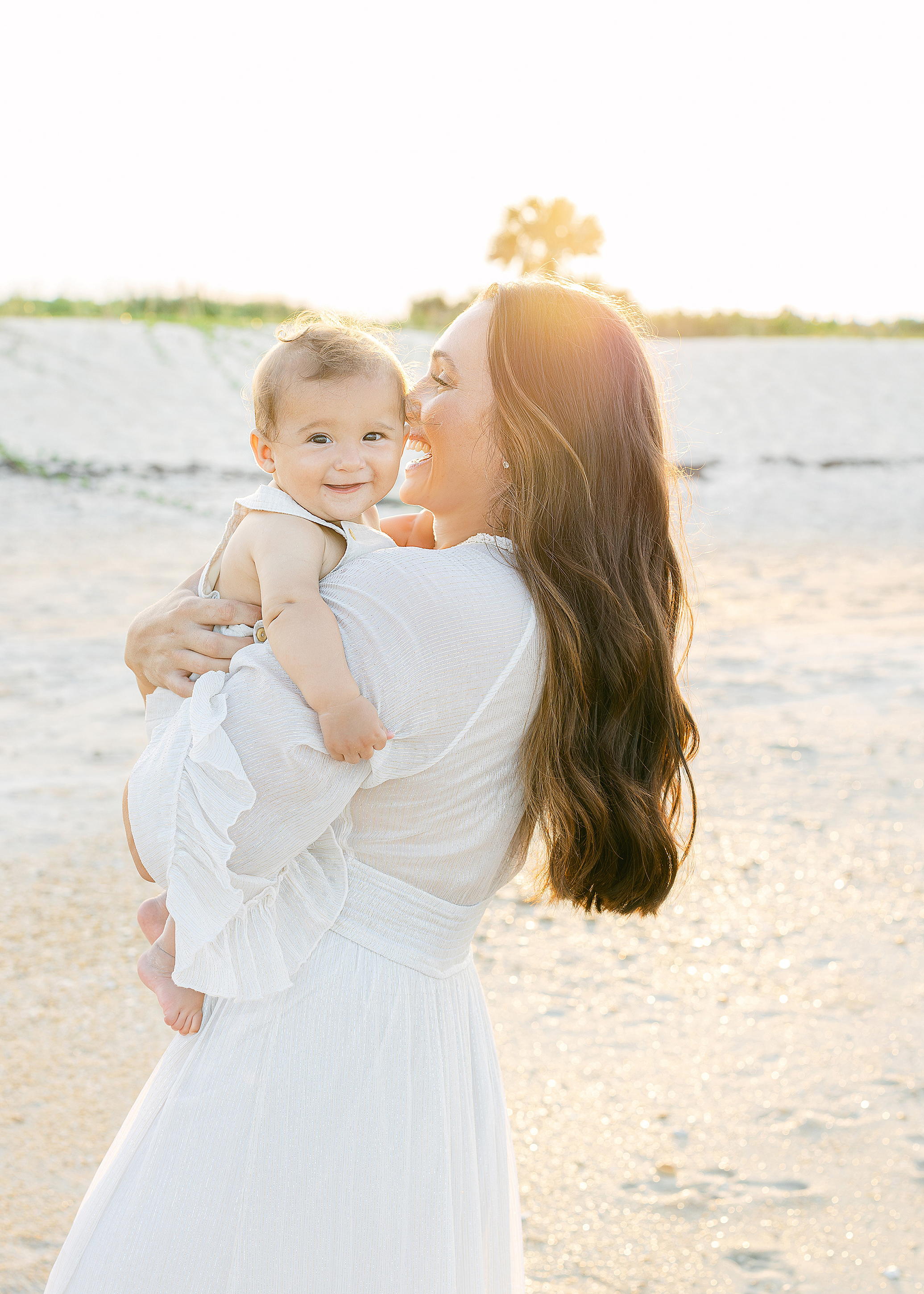 A sunset motherhood portait of woman on the beach with her baby boy.