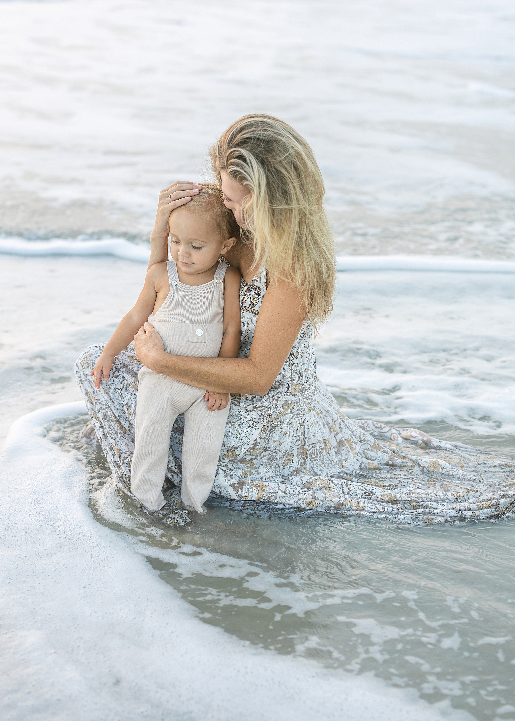 A mother sits in the surf on the beach at sunrise with her baby boy in St. Augustine.