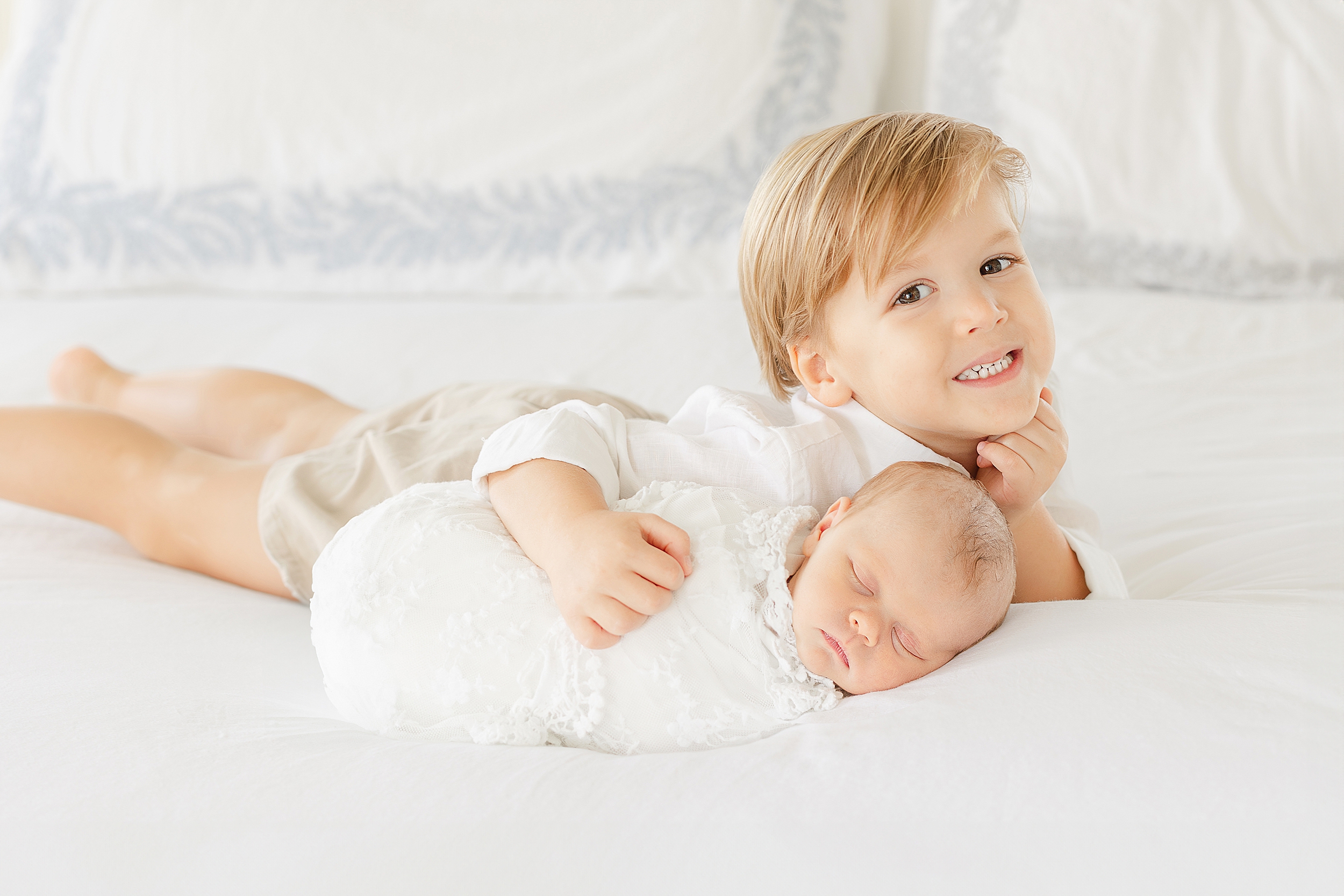 A toddler boy holds his newborn baby sister during an in-home newborn portrait session.