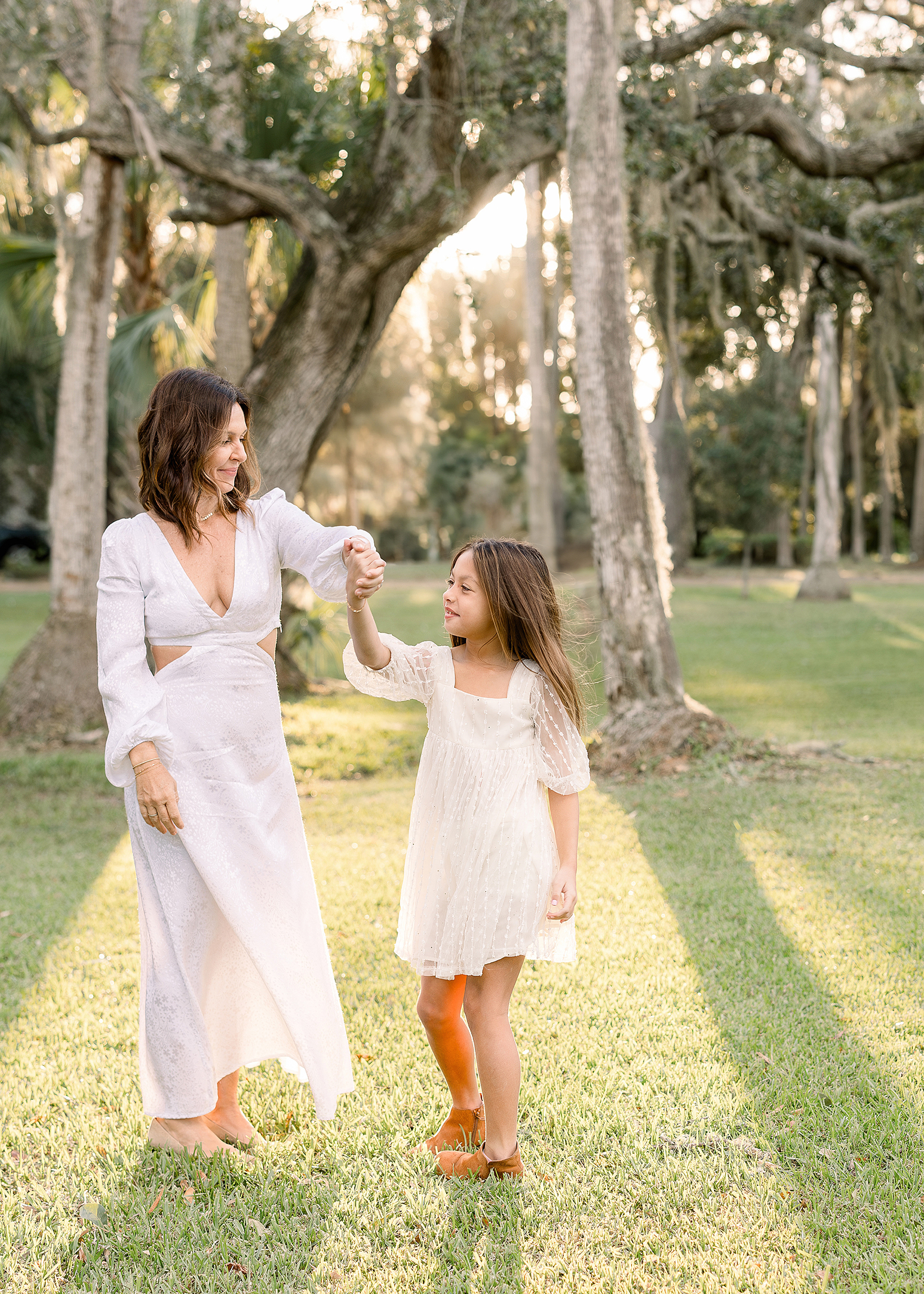 A mother and daughter in white dresses twirl together in the sunlight at Johansen Park in Atlantic Beach, FL.