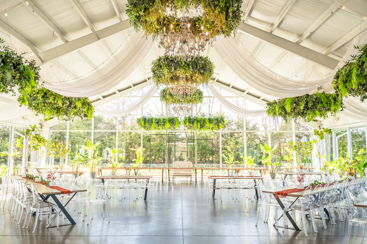 Glass wedding venue set with tables and ghost chairs for a wedding reception.