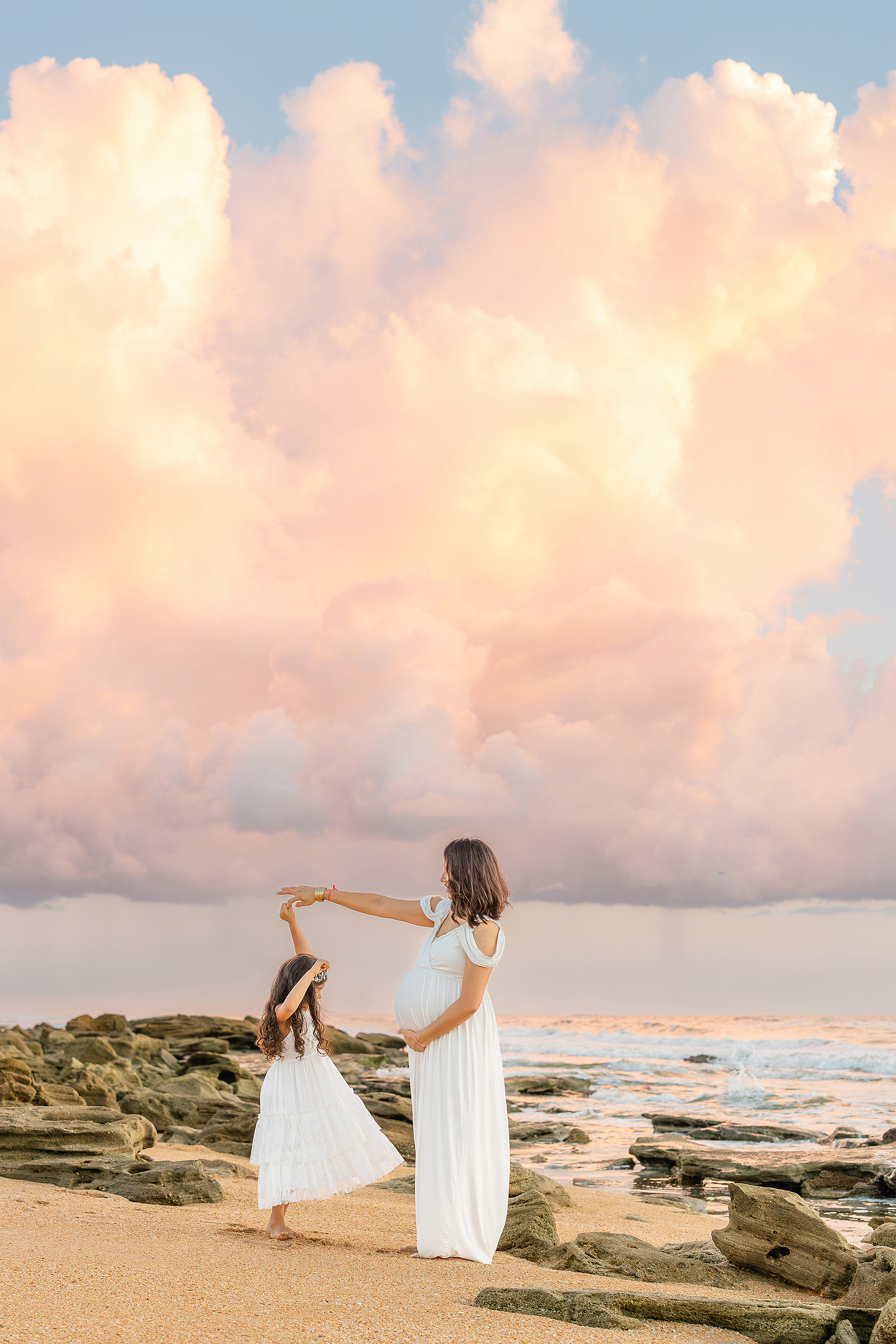 A colorful sunrise portrait of a mother and her daughter twirling on the beach.