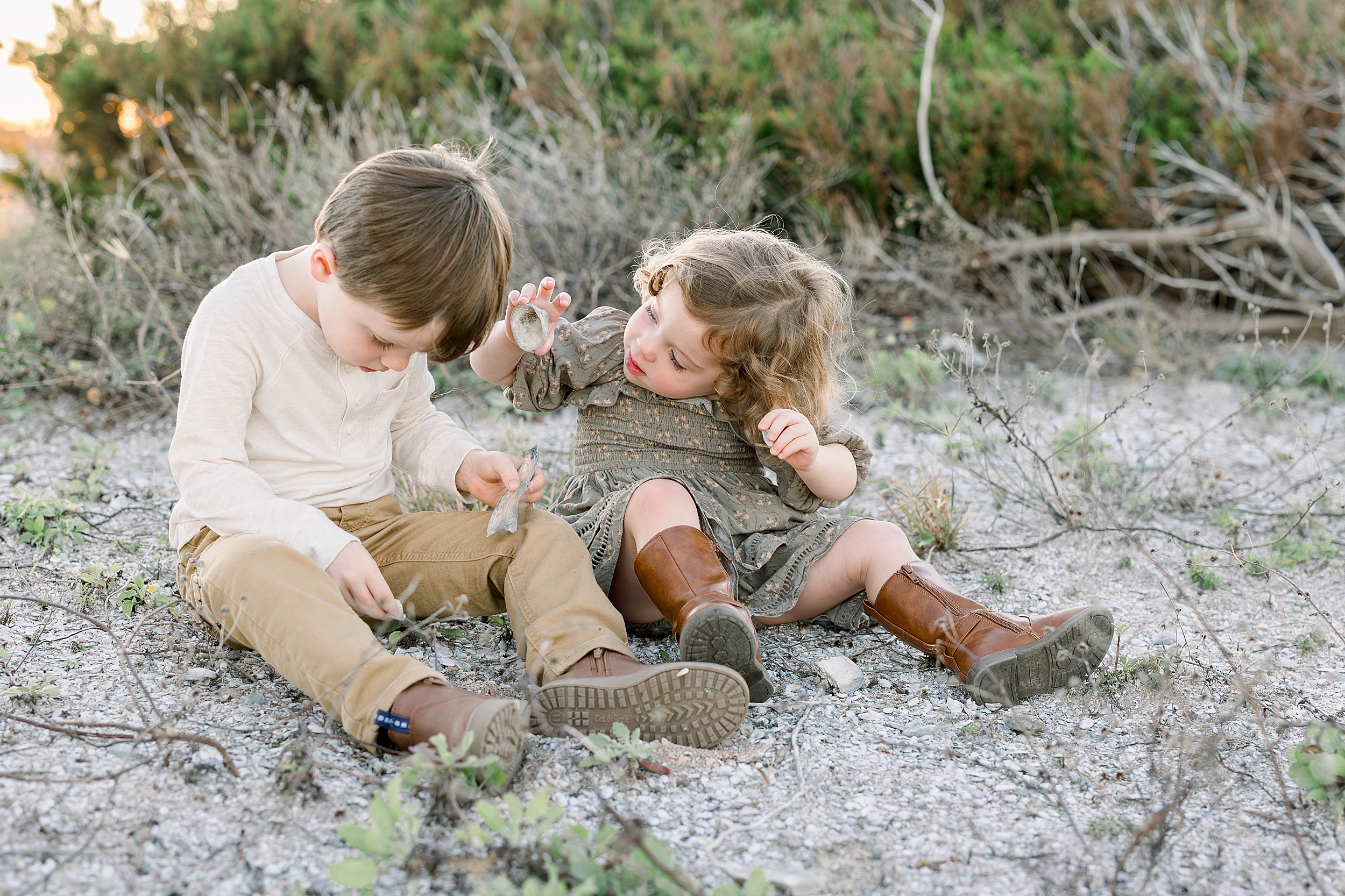 Two little children sit together on the ground and play with shells.