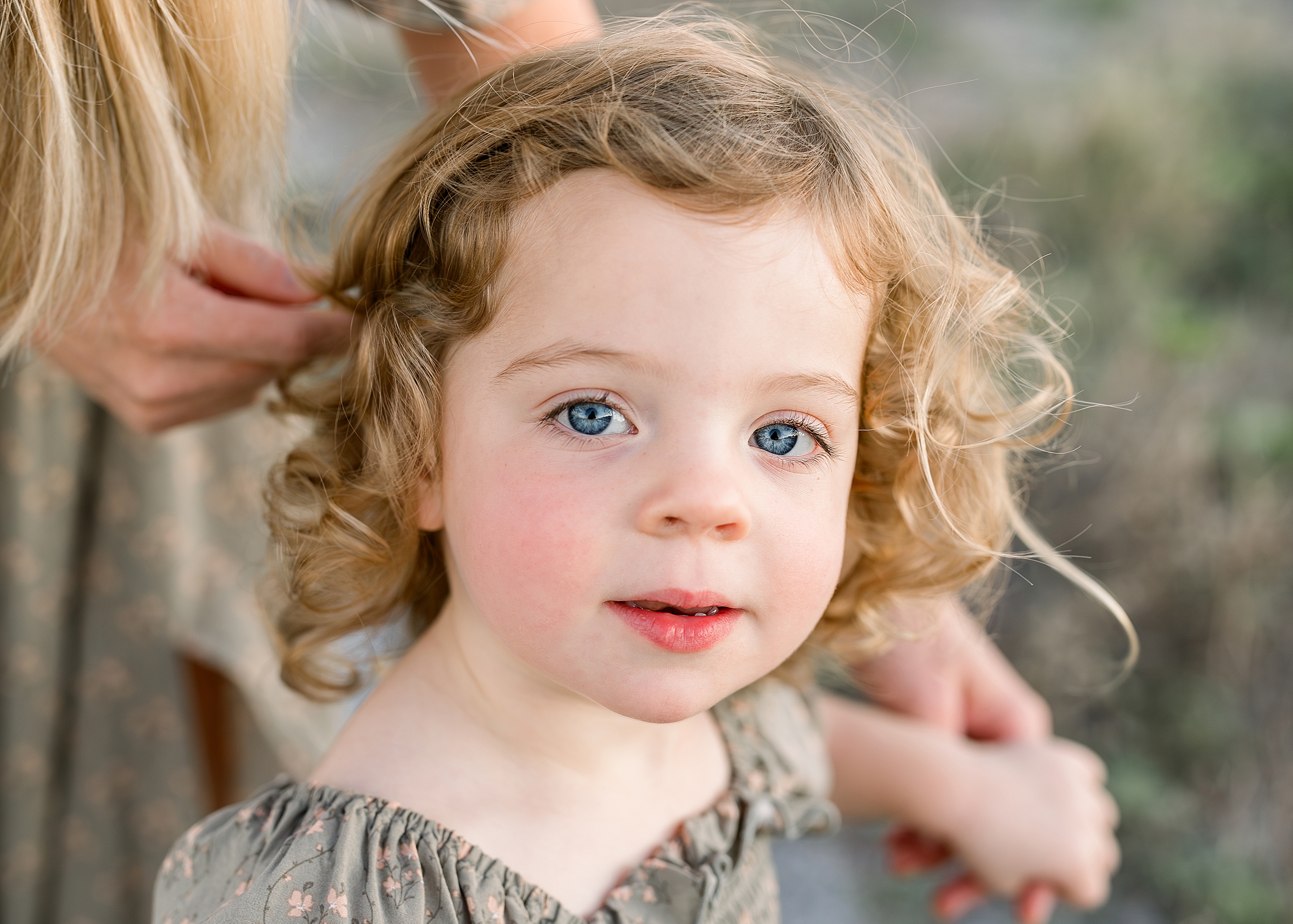 A portrait of a little girl with blue eyes and brown hair stares into the camera wearing a sage green dress.