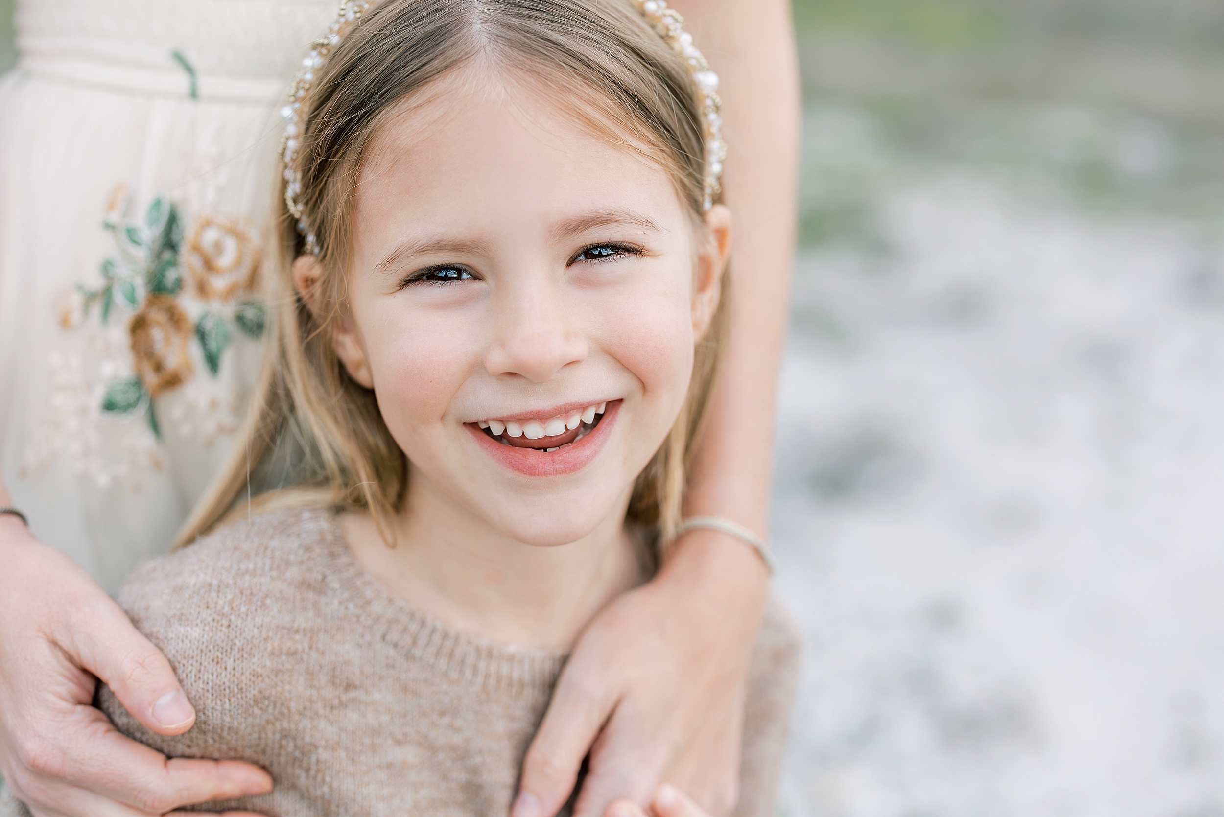 A portrait of a little girl in a taupe dress and a rhinestone headband.