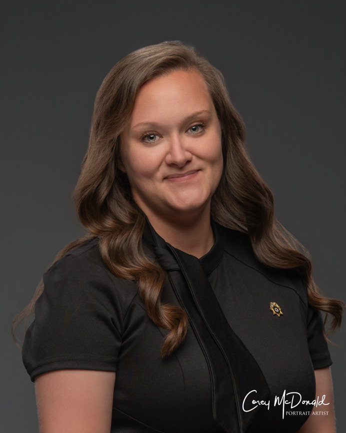 Smiling person with long wavy hair wearing a black shirt, set against a dark background.