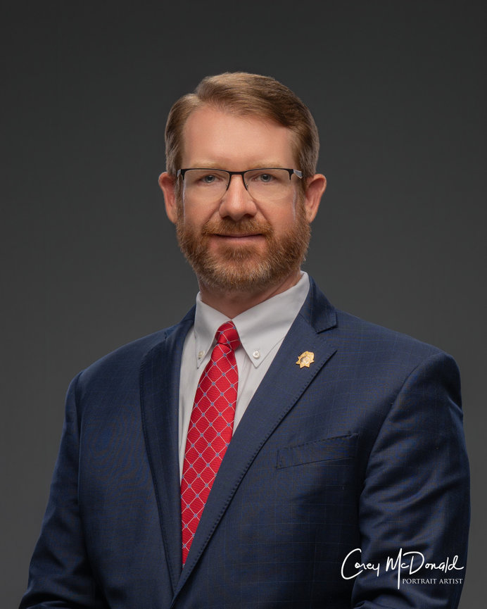 Man with glasses in a suit and red tie, posing against a gray background.