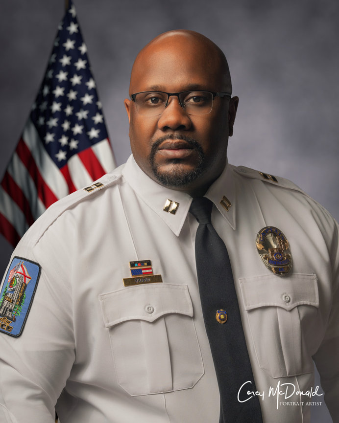 A police officer in uniform poses in front of an American flag.