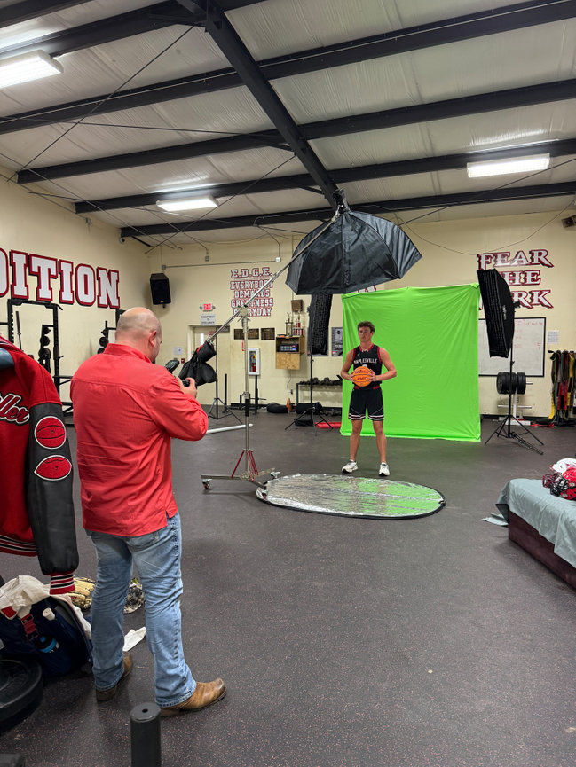 Photographer in a gym taking a photo of a person in front of a green screen with lighting equipment.