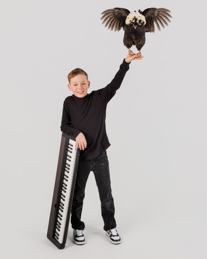 Boy posing with a keyboard and balancing a bird on his raised hand against a white background