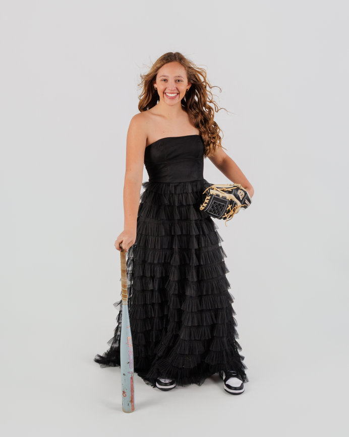 Smiling young woman in a black dress holding a softball bat and glove on a white background
