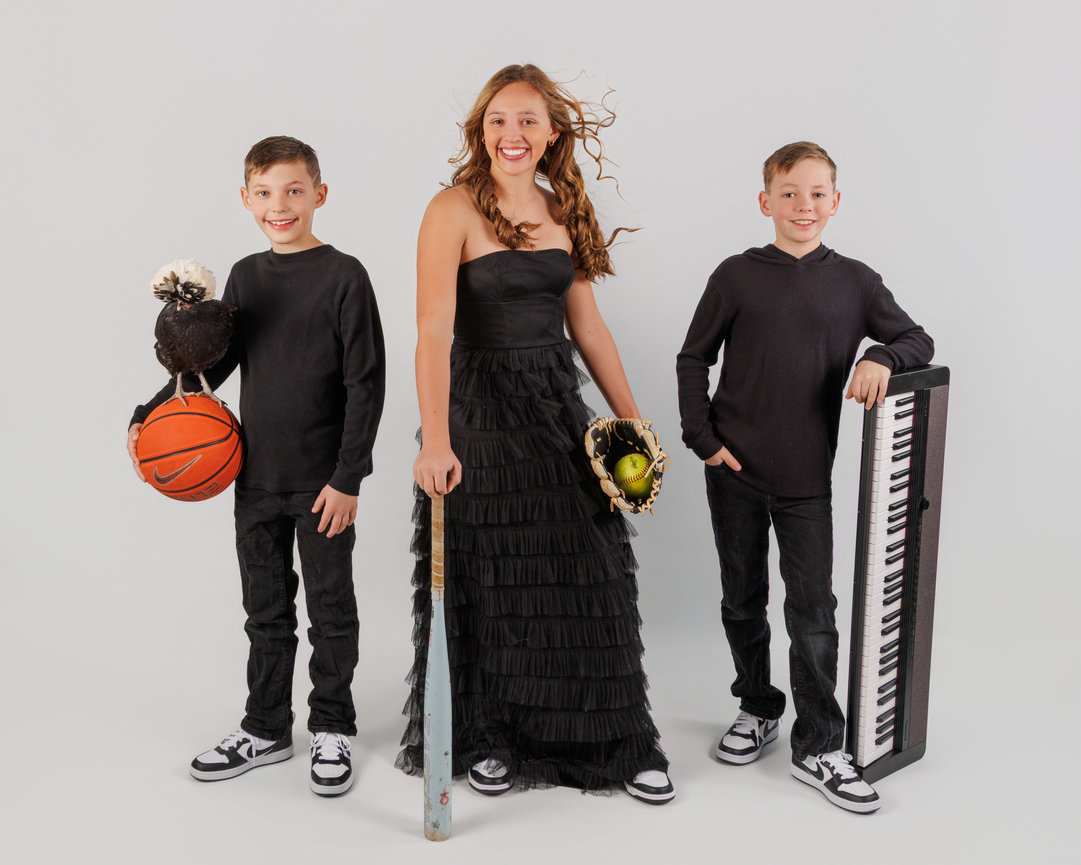 Three smiling youths in black outfits posing with sports and music props on a white background