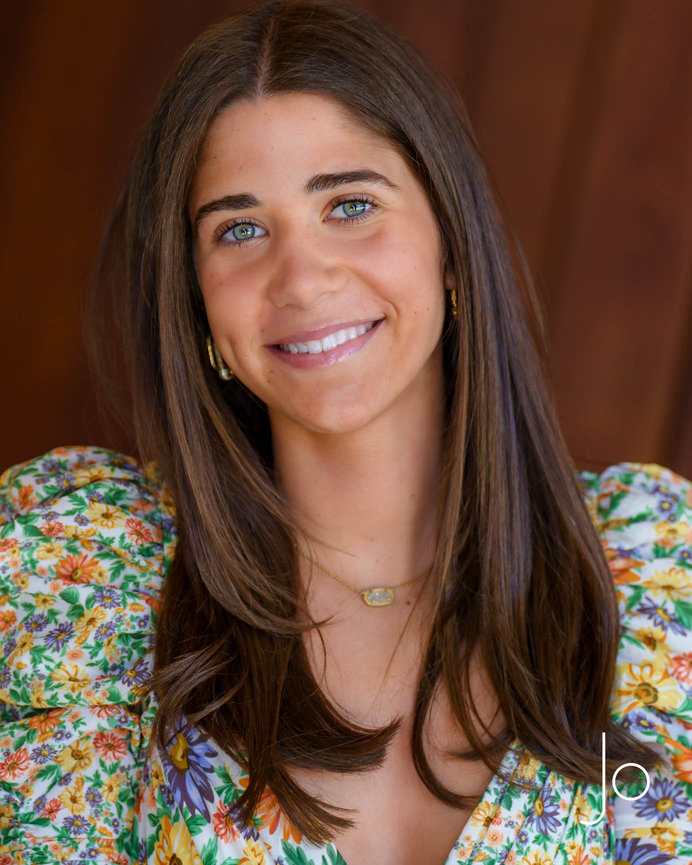 Smiling teen with long hair wearing a floral-patterned top against a brown background.