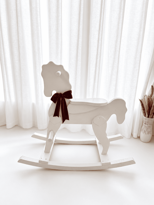 White rocking horse with a burgundy ribbon bow