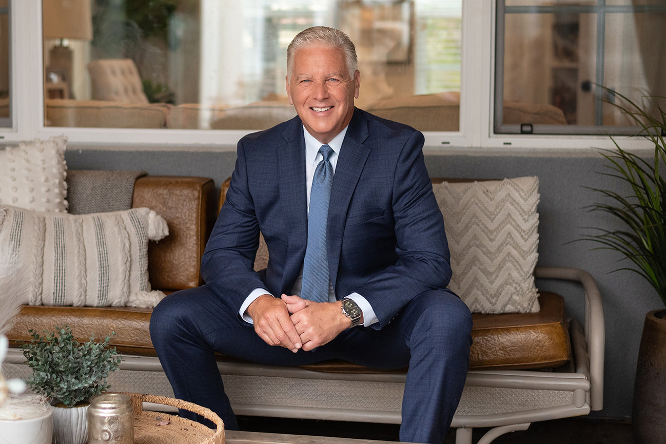 Distinguished gentleman and smiling realtor in suit and tie, seated on leather sofa, by San Diego Personal Branding Photographer, Stefanie Blue.