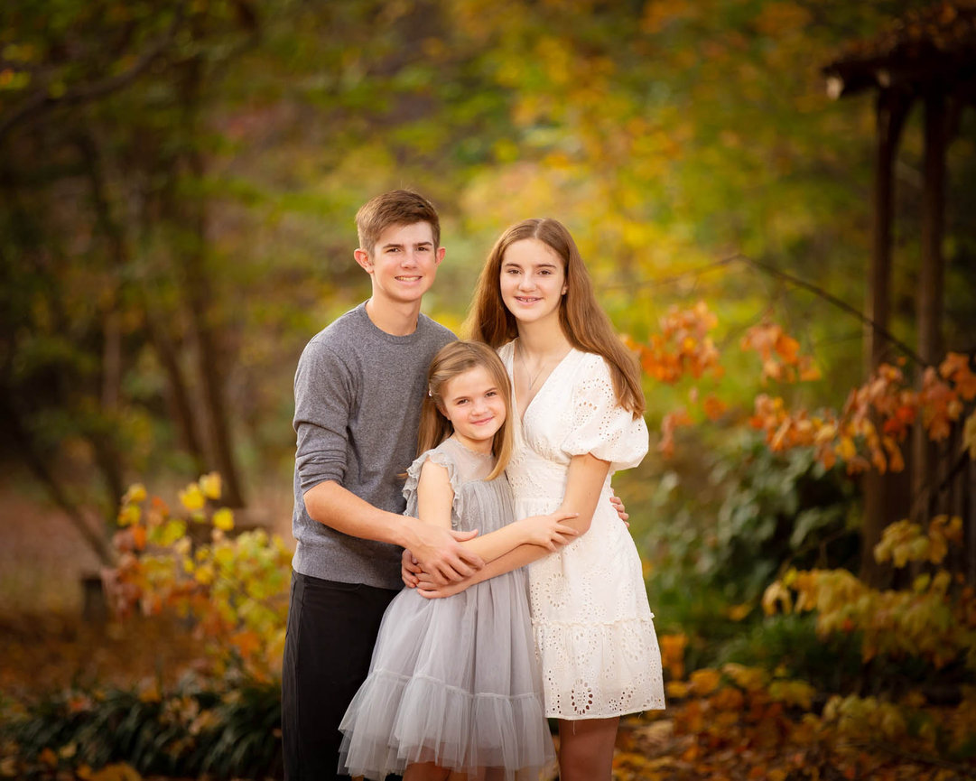 Classic sibling portrait with coordinated outfits and natural smiles, posed in a soft outdoor setting.
