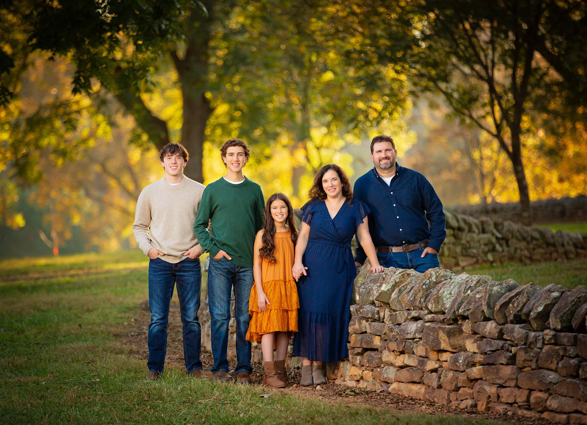 Family of five standing before a rustic stone wall, photographed in natural light with a classic, elegant composition.