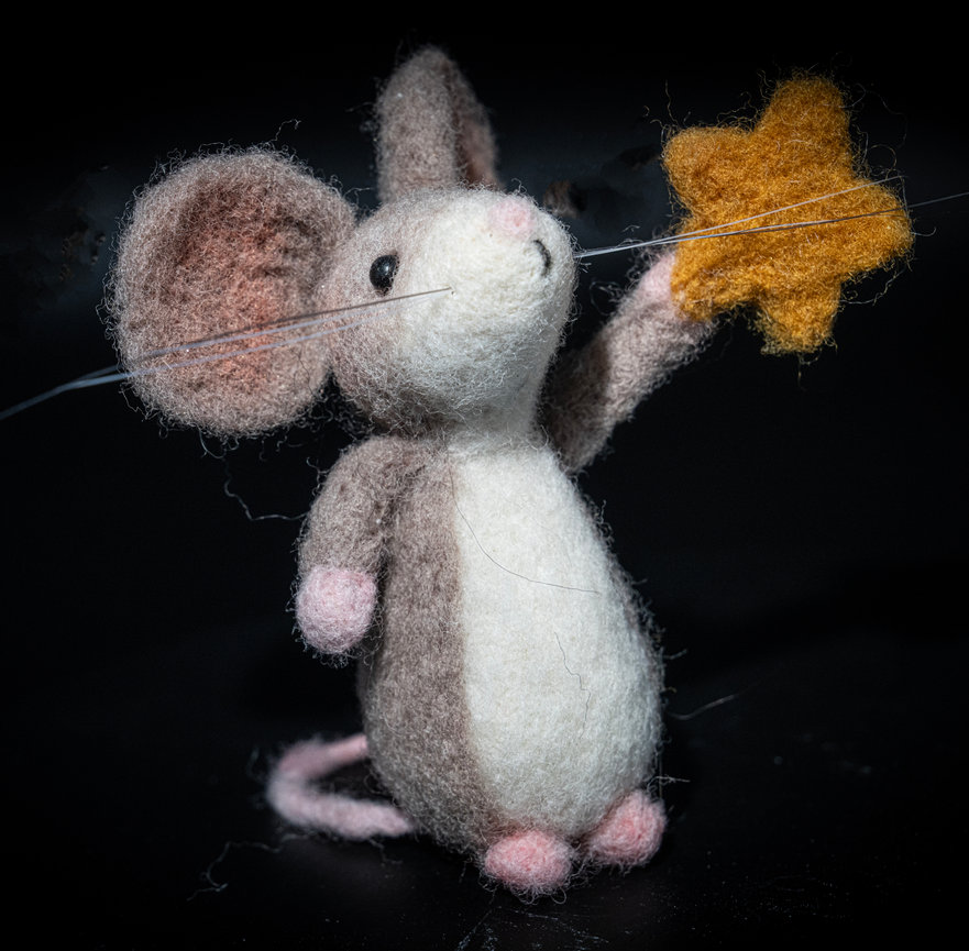 Needle-felt mouse holding an orange star-shaped treat on a black background