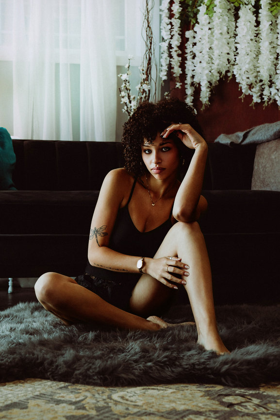 Woman sitting on a rug in a dark living room with floral decor and soft window light