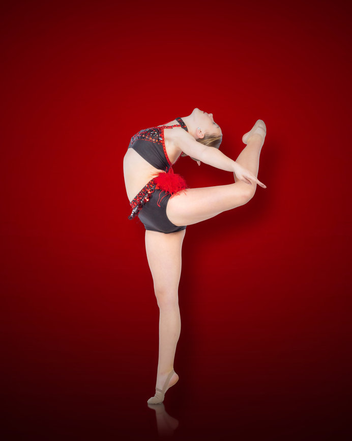 Dancer in a red and black outfit performs a ballet pose against a red background.