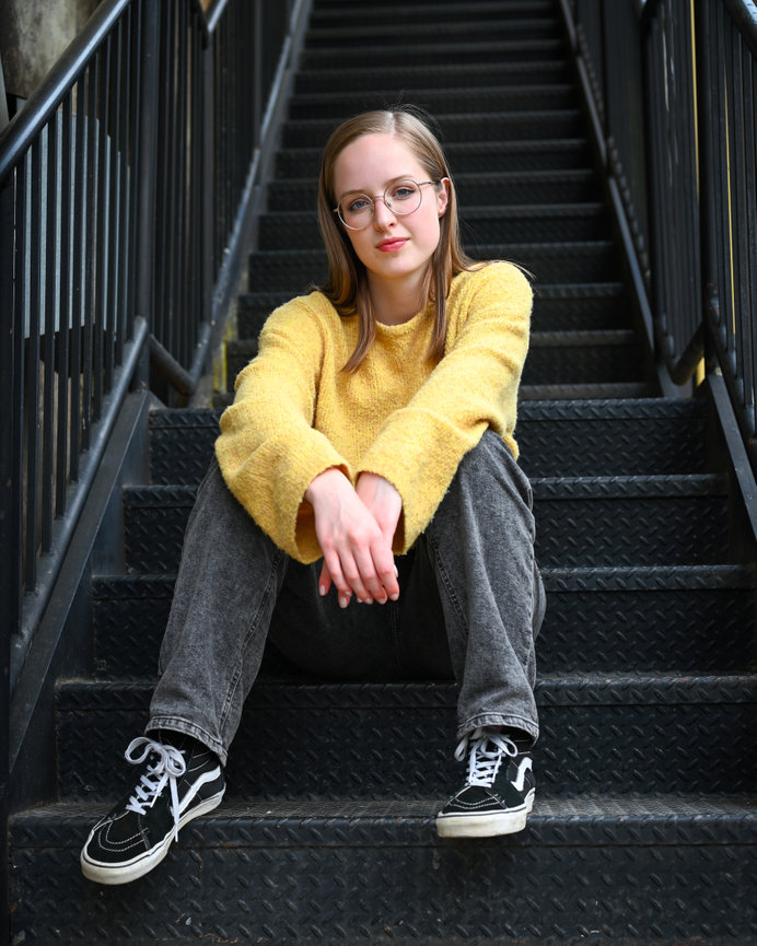 Young woman in a yellow sweater and glasses sitting on black metal stairs
