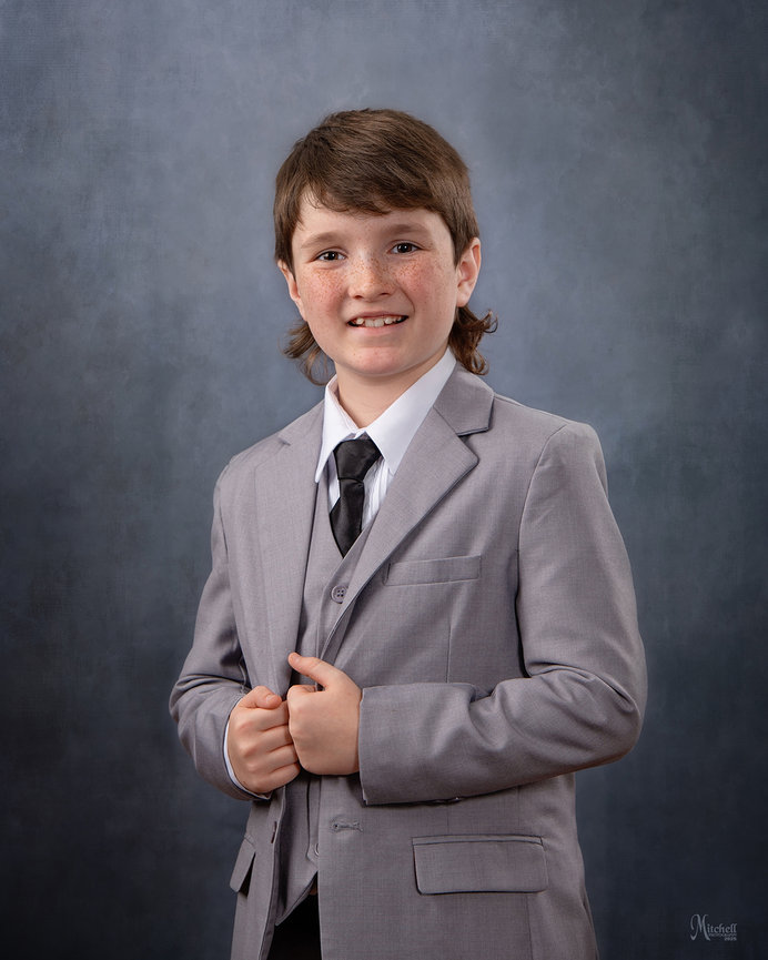 Young boy in a gray suit and black tie posing for a studio portrait