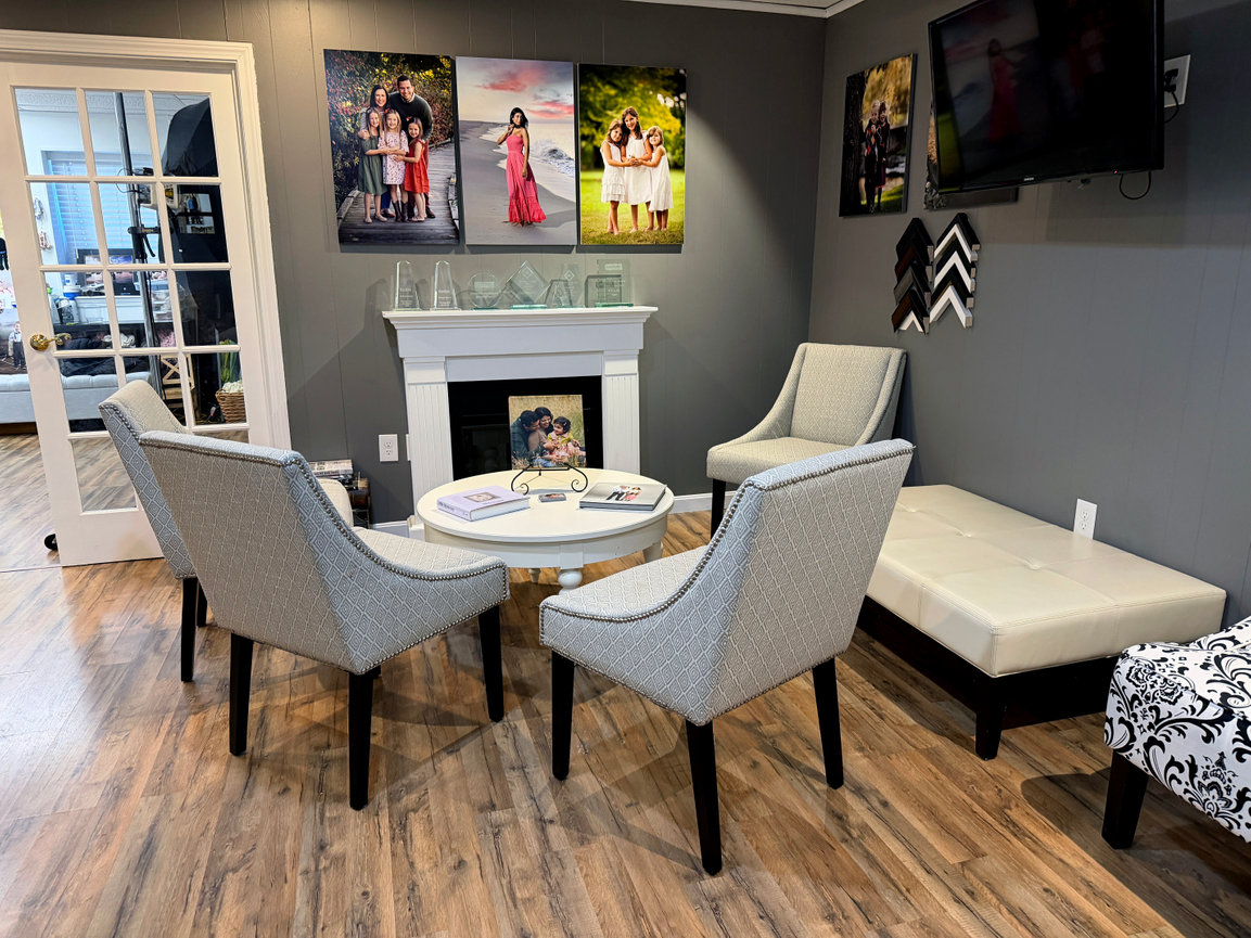 Cozy waiting room in Paula Swift Photography studiowith gray chairs, framed photos on walls, and a fireplace.