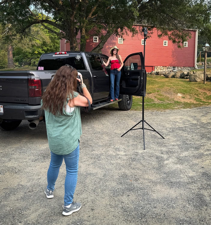 Photographer captures high school senior posing by truck in front of red barn at Wayside Inn..