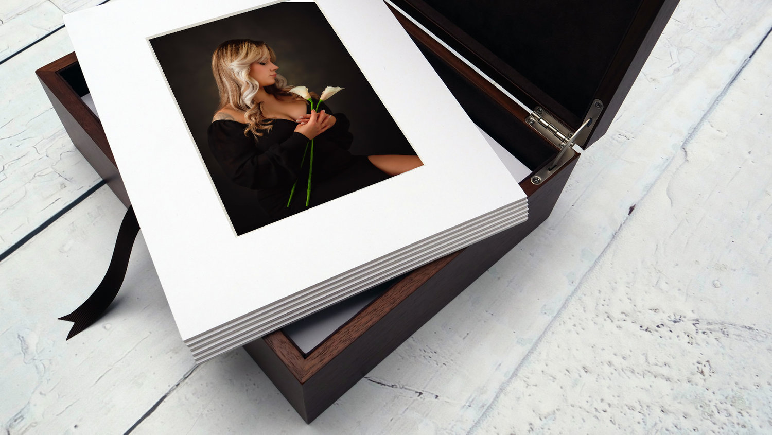 Matted photos in a wooden box on a white wooden surface, featuring a woman holding a calla lily.