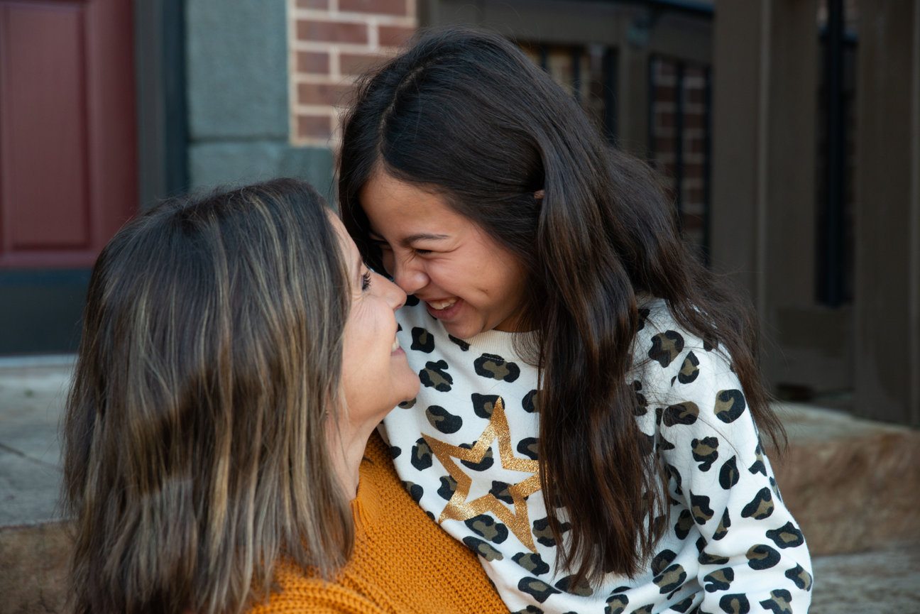 Mother and daughter smiling and leaning close outside a home.