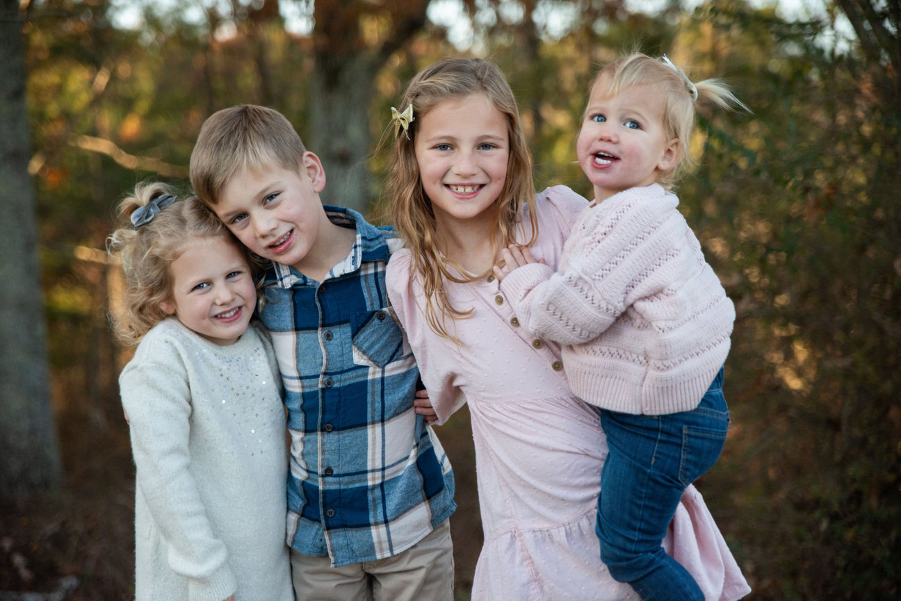 Family of four posing together outdoors in soft light.