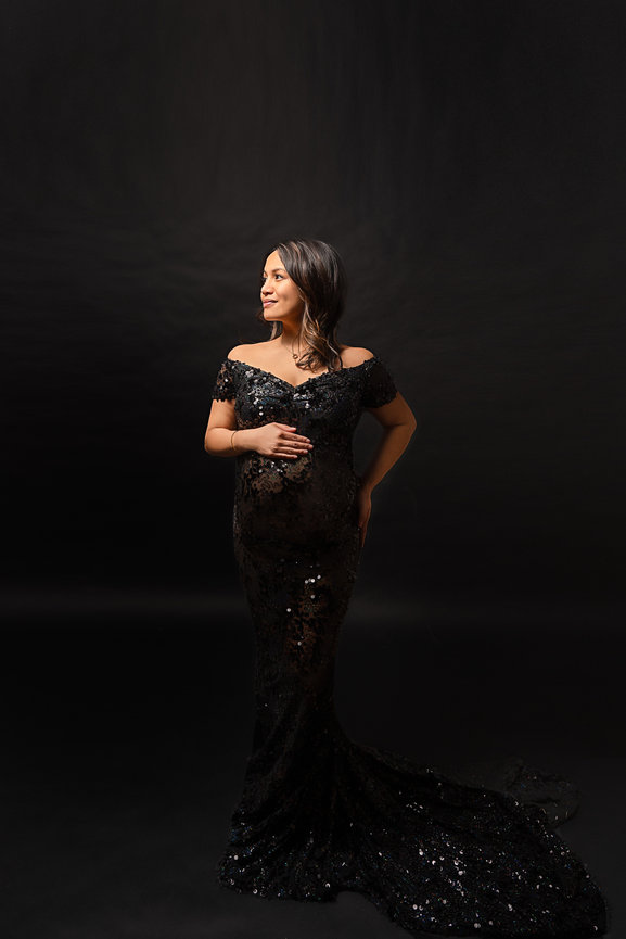 Luxury maternity portrait with expectant mother in beaded gown and side-lit backdrop.