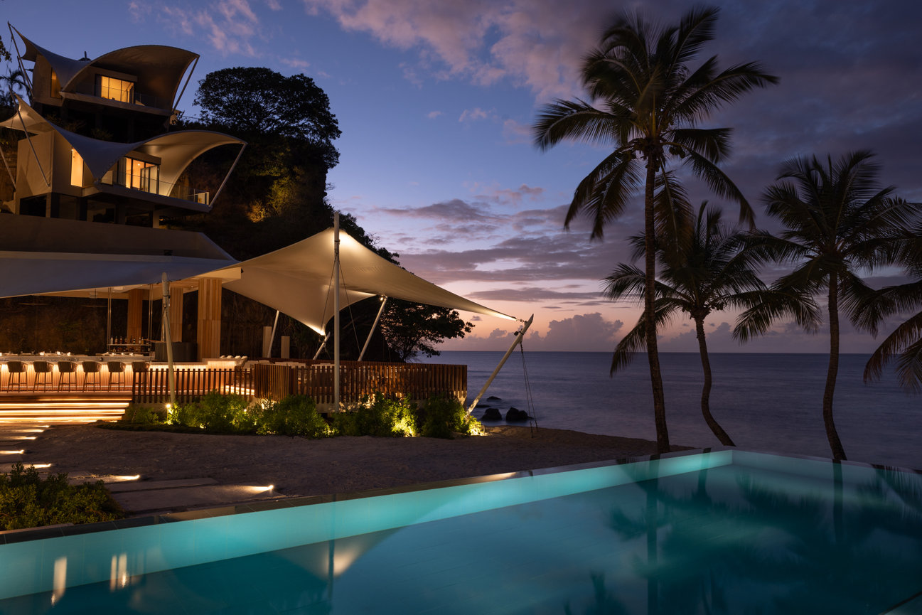 Hotel in Grenada with beautifully lit pool and outdoor restaurant on the ocean at sunset.