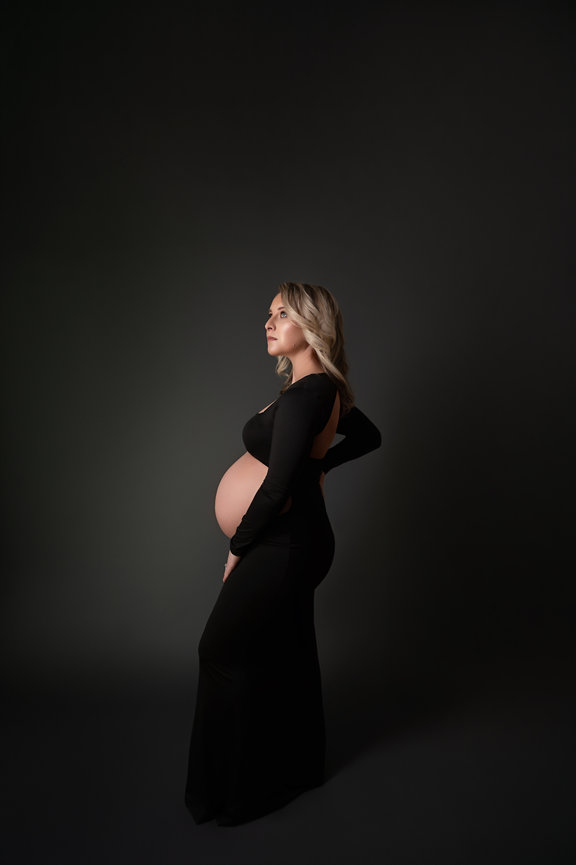 Fashion-forward maternity photo of mom in cutout dress with dramatic lighting.