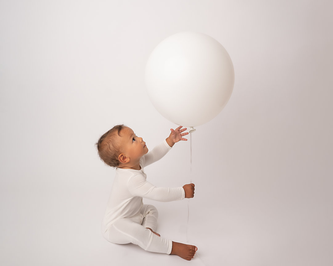 One-year-old smiling on white backdrop in Point Pleasant holding oversized white balloon