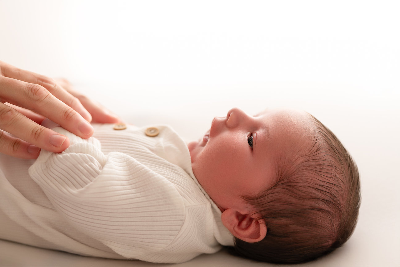 Parent’s hand cradles baby’s hands in white studio light