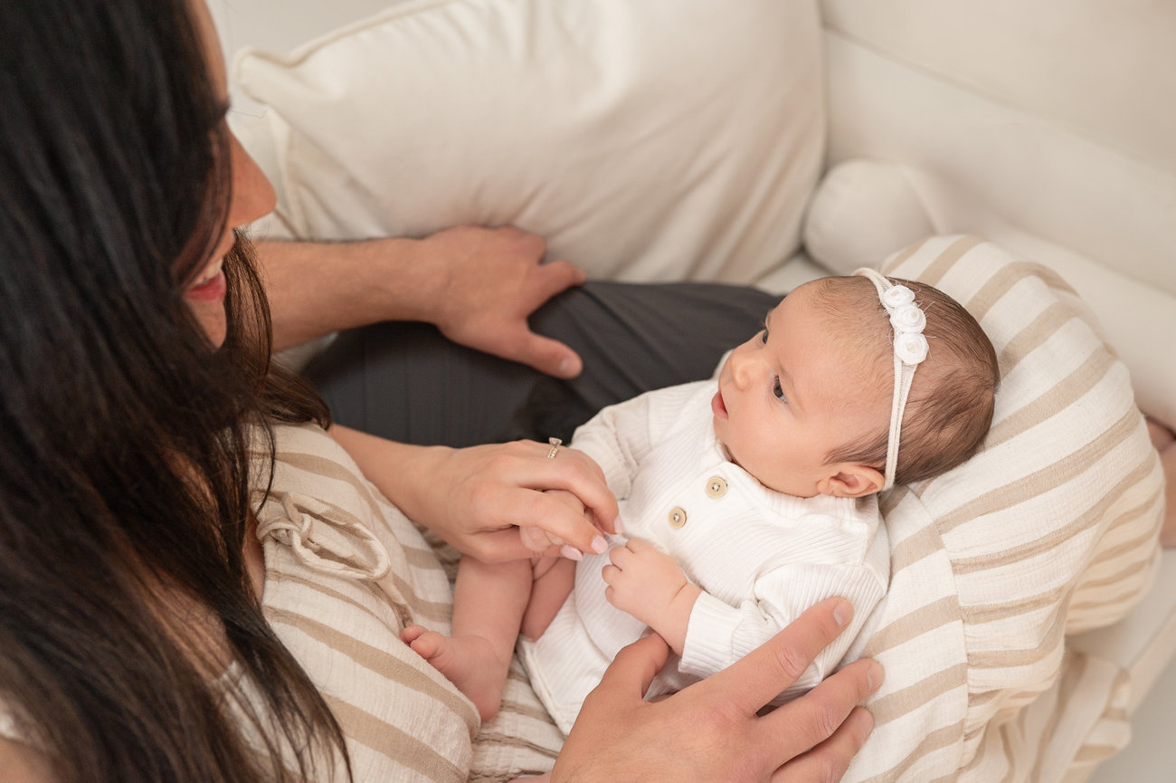 Baby nestled safely in both parents’ arms, captured in clean, minimalist setting in Kristin Baker’s Holmdel studio