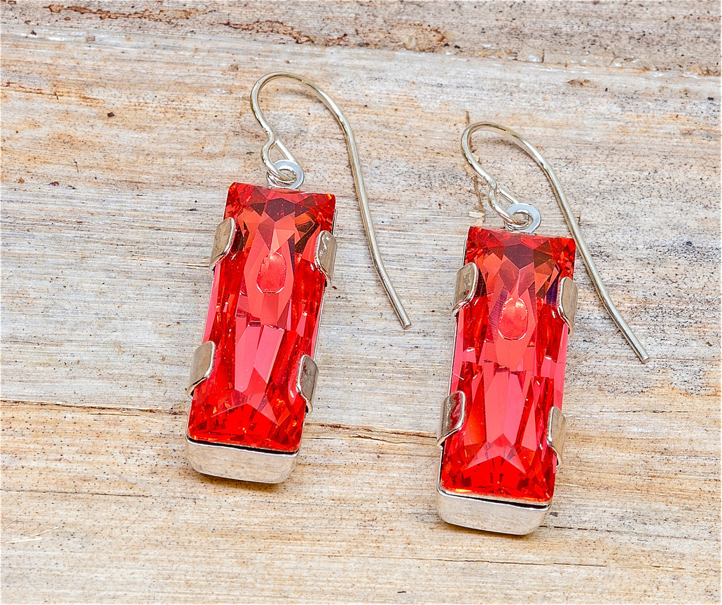 Pair of silver dangle earrings featuring elongated rectangular-cut red gemstones in four-prong settings, displayed on a rustic wooden background